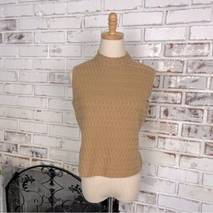May include: A sleeveless, mock neck sweater in a light brown color. The sweater has a textured knit pattern.