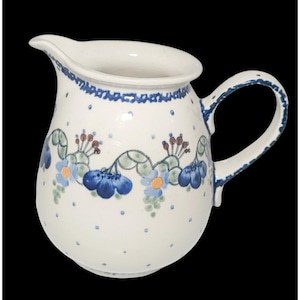 Könnte beinhalten: Ein cremefarbener Keramikkrug mit einem handgemalten Blumenmuster aus blauen Blütenblättern, gelben Mitten und grünen Stielen. Das Design umfasst kleine blaue Punkte, die über die Oberfläche verteilt sind, sowie einen blauen Rand am oberen Teil.