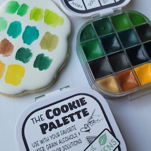 May include: A cookie palette with green watercolor paints and a variety of colors. The palette includes a cookie with green paint swatches, a container of green paints, and a container with color names like "Leaf Green" and "Mint Green".