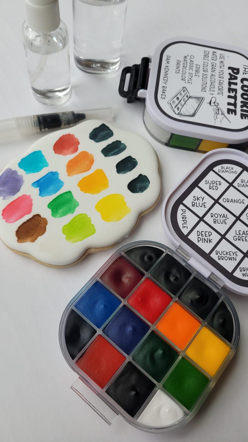 May include: A cookie palette with various edible watercolor paints. The palette includes a variety of colors, such as red, blue, green, and yellow. Also included are two bottles of liquid and a brush.