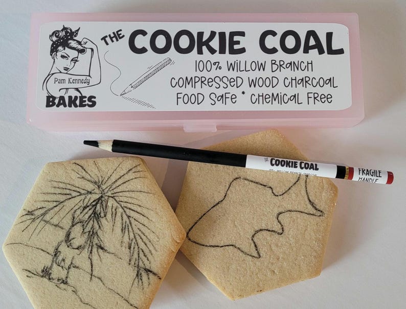Peut inclure: Une bo&icirc;te rectangulaire rose avec le texte "THE COOKIE COAL" et "Pam Kennedy BAKES" est au-dessus de deux biscuits d&eacute;cor&eacute;s et d'un crayon noir. Le crayon est &eacute;tiquet&eacute; "COOKIE COAL" et "FRAGILE HANDLE". Les biscuits ont des dessins dessus.