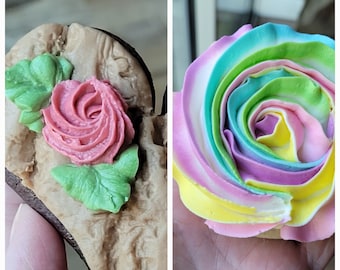 May include: Close-up of two decorated biscuits. One is heart-shaped with a pink rose and green leaves. The other is a rainbow-coloured swirl, resembling a rose. Both are held in a hand.