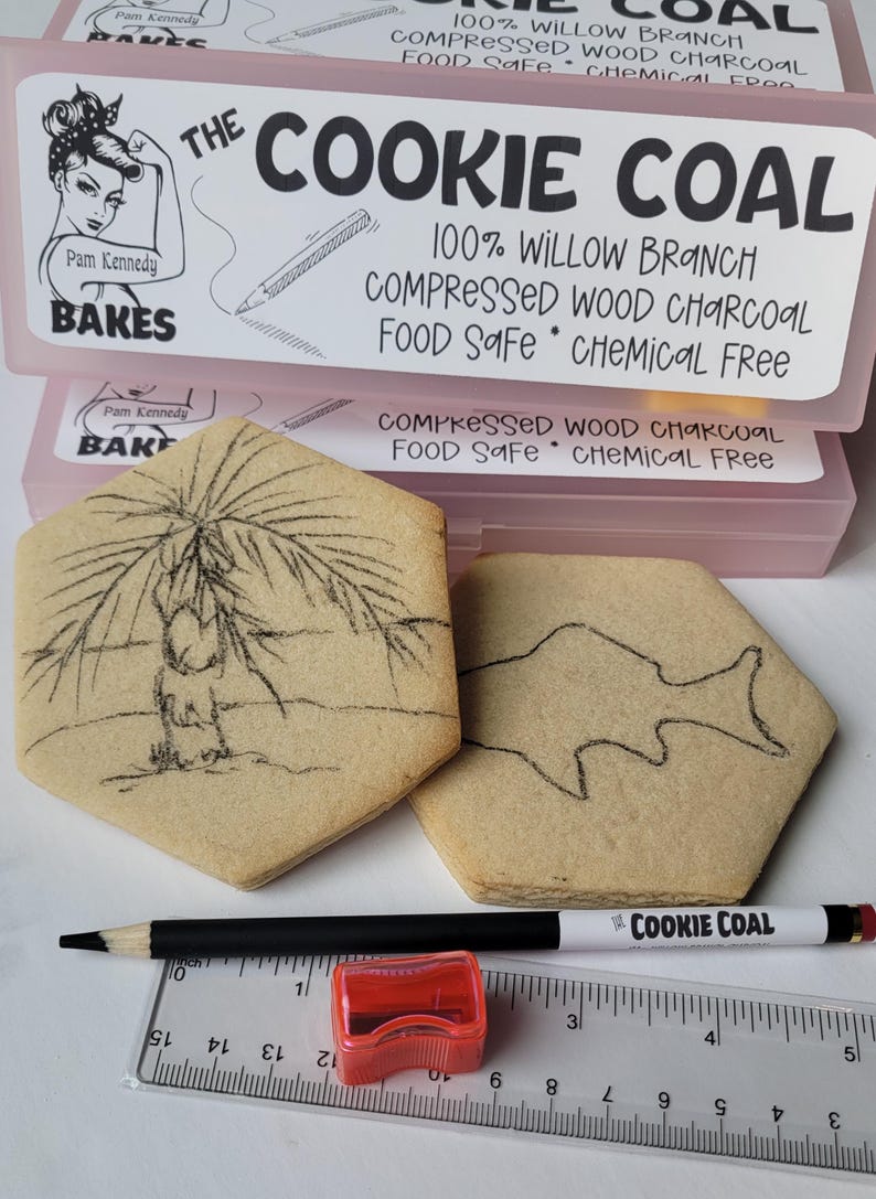 Peut inclure: L'image pr&eacute;sente des biscuits hexagonaux avec des dessins au fusain d'un palmier et d'un poisson. Un crayon, un taille-crayon et une r&egrave;gle sont &eacute;galement pr&eacute;sents. L'emballage indique "The Cookie Coal" et "Food Safe".