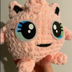 Puede incluir: Un personaje rosa de peluche hecho a mano, con ojos grandes y expresivos y brazos y piernas pequeños. El personaje tiene detalles negros en las orejas y una boca sonriente. El texto "Pattern only" está en la parte superior.