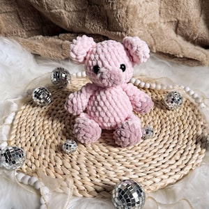 May include: A pink crocheted pig plush toy sitting on a woven straw mat with silver disco ball decorations.
