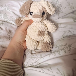 K&ouml;nnte beinhalten: Ein handgefertigtes Stofftier in Form eines Hundes mit cremefarbenen und braunen Akzenten. Der Hund hat Schlappohren, eine kleine Nase und dunkle Augen. Das Spielzeug besteht aus einem weichen, strukturierten Material.