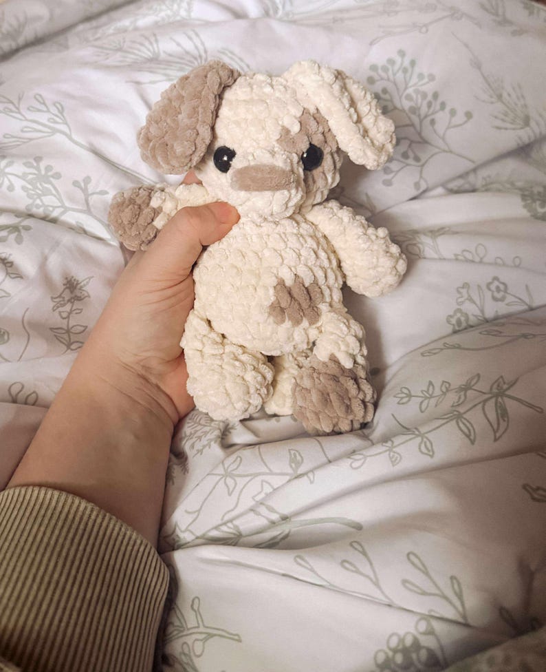 K&ouml;nnte beinhalten: Ein handgefertigtes Stofftier in Form eines Hundes mit cremefarbenen und braunen Akzenten. Der Hund hat Schlappohren, eine kleine Nase und dunkle Augen. Das Spielzeug besteht aus einem weichen, strukturierten Material.