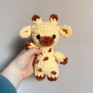 Puede incluir: Un juguete de peluche de jirafa tejido a crochet con manchas marrones y un cuerpo amarillo. La jirafa tiene ojos negros y una nariz marrón.