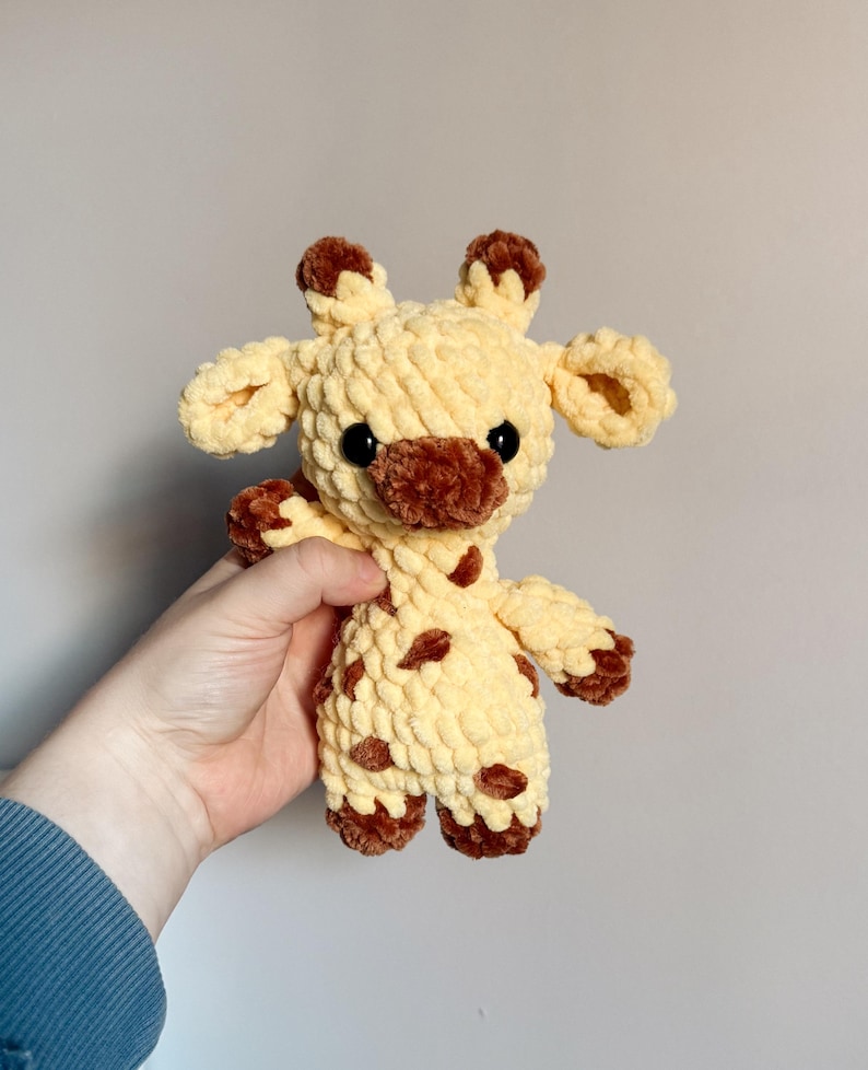 May include: A crocheted stuffed giraffe toy with brown spots and a yellow body. The giraffe has black eyes and a brown nose.