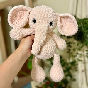 May include: A pink crocheted elephant plush toy with black eyes. The elephant has a long trunk and floppy ears.