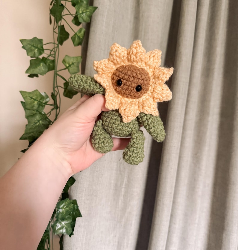 K&ouml;nnte beinhalten: Ein geh&auml;keltes Pl&uuml;sch-Sonnenblumenspielzeug mit braunem Gesicht und schwarzen Augen. Die Sonnenblume ist gelb und orange mit gr&uuml;nen Bl&auml;ttern.