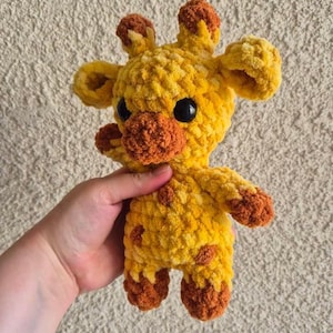 May include: A crocheted yellow and orange giraffe stuffed animal with black eyes.