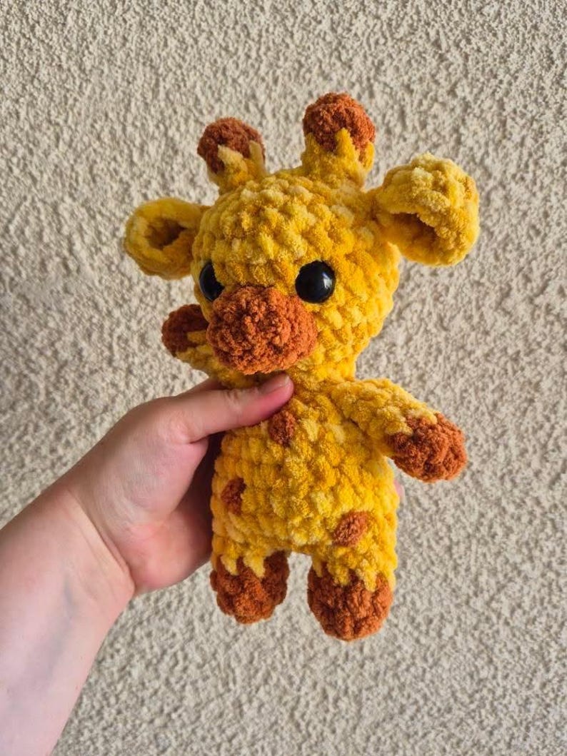May include: A crocheted yellow and orange giraffe stuffed animal with black eyes.