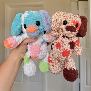 K&ouml;nnte beinhalten: Zwei handgefertigte Hunde-Pl&uuml;schtiere aus H&auml;kelarbeit. Eines ist blau, wei&szlig;, rosa und orange. Das andere ist braun, orange und rot. Beide haben schwarze Augen und Schlappohren. Die Pl&uuml;schtiere sind weich und kuschelig.