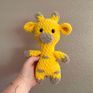 May include: A yellow crocheted giraffe stuffed animal with brown ears, nose, and feet. The giraffe has black eyes and a textured, fuzzy surface.