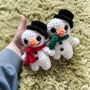 May include: Two white crocheted snowman ornaments with black hats and buttons. One snowman has a red scarf and the other has a green scarf.