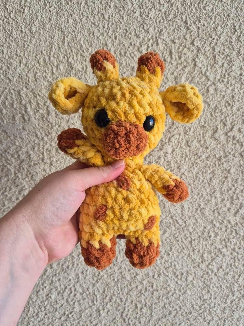 May include: A crocheted giraffe stuffed animal with brown spots and a brown nose. The giraffe is yellow and has black eyes.
