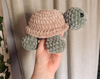 Puede incluir: Una tortuga de ganchillo hecha a mano con hilo suave y afelpado. La tortuga presenta un caparazón marrón claro, una cabeza verde y patas verdes. Un juguete tierno y caprichoso.