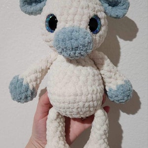 May include: A crocheted stuffed animal in the shape of a giraffe with white fur, blue ears, and blue hooves. The giraffe has large blue eyes with glitter.