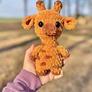 May include: A crocheted giraffe plush toy with brown and orange fur. The giraffe has large black eyes and a brown nose.