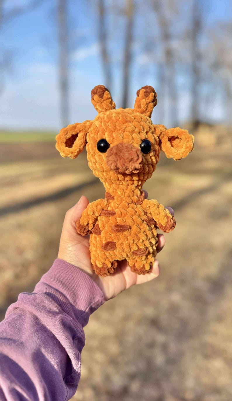 May include: A crocheted giraffe plush toy with brown and orange fur. The giraffe has large black eyes and a brown nose.