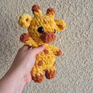 May include: A crocheted giraffe stuffed animal with yellow and brown yarn. The giraffe has a brown nose and black eyes.