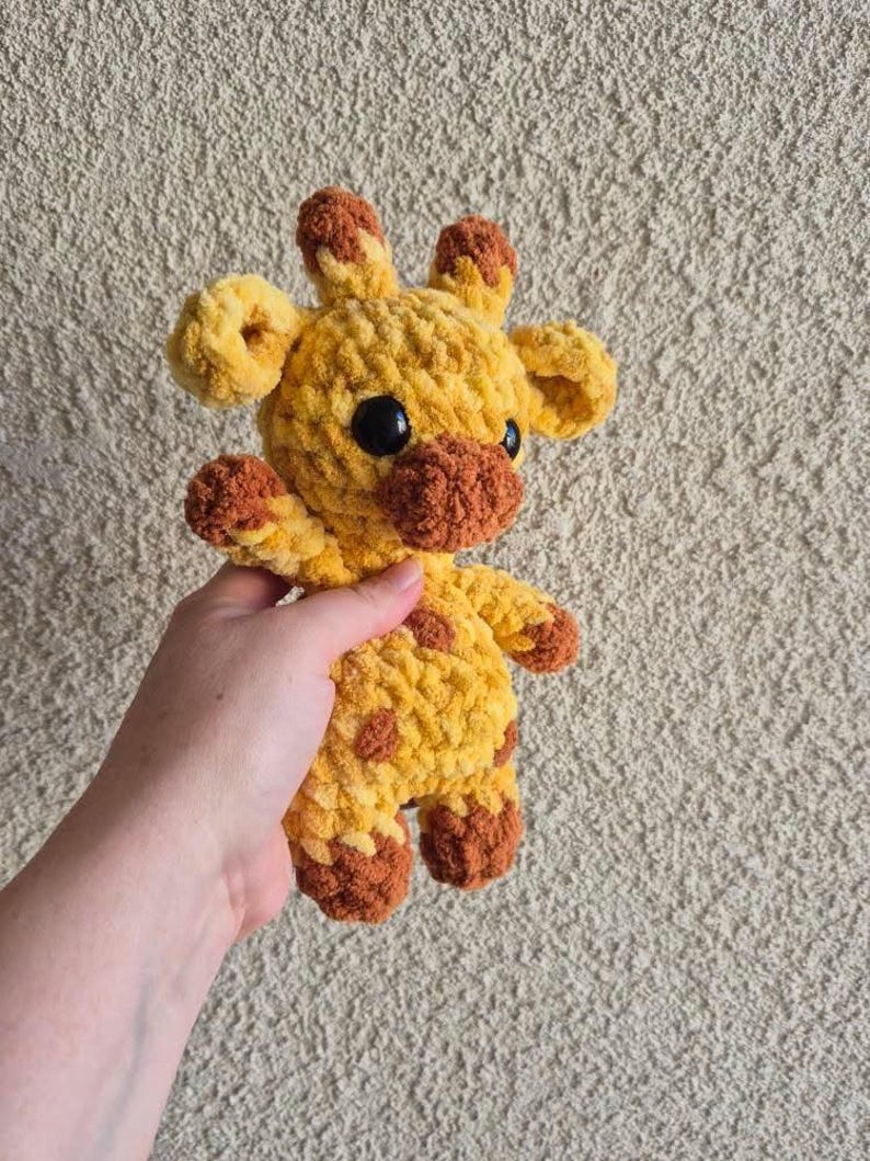 May include: A crocheted giraffe stuffed animal with yellow and brown yarn. The giraffe has a brown nose and black eyes.