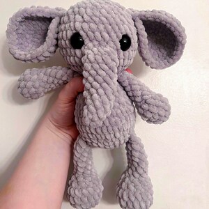 May include: A gray crocheted elephant plush toy with black eyes. The elephant has a long trunk and floppy ears.