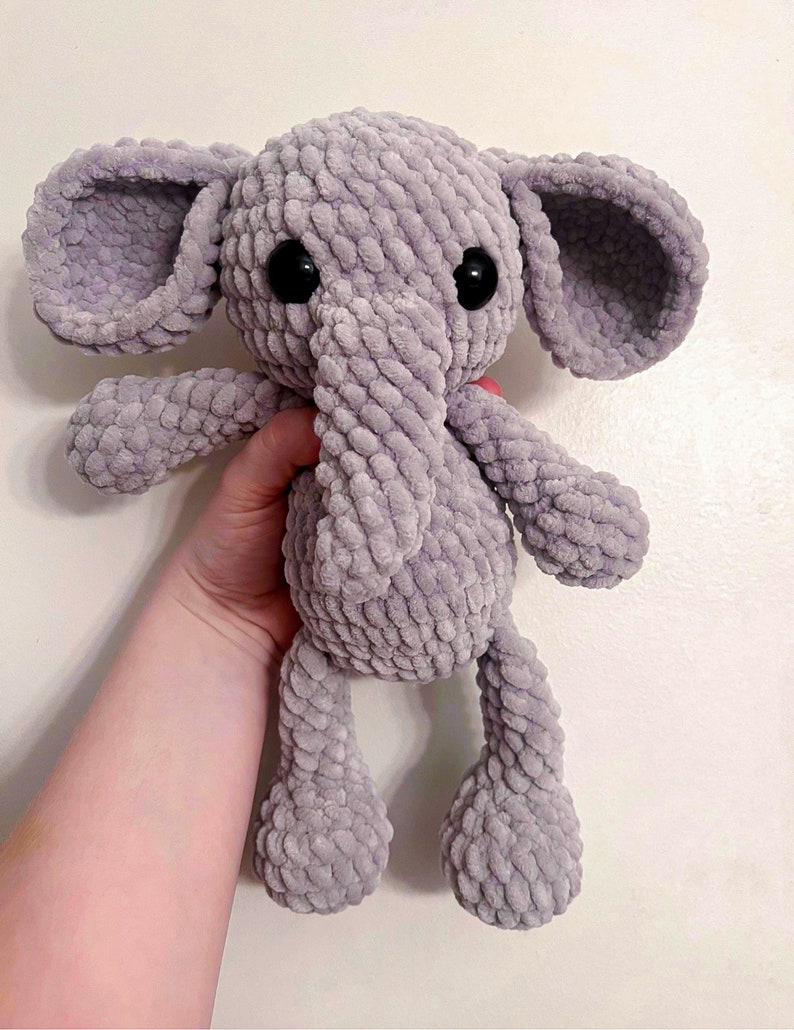 May include: A gray crocheted elephant plush toy with black eyes. The elephant has a long trunk and floppy ears.