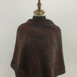 May include: A brown paisley patterned scarf with a green and red design. The scarf has the word "BALMAIN" printed on the bottom corner.