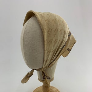 May include: A tan bandana with a brown logo pattern and the word "CHAMP" printed on the edge. The bandana is tied around a mannequin head.