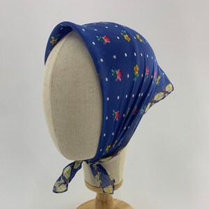 May include: A blue and white polka dot headscarf with a floral print. The scarf is tied on a mannequin head.