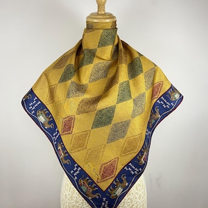 May include: A square scarf featuring a yellow and green diamond pattern across the center. The border is a deep blue color decorated with illustrations of elephants in ornate saddles and small white symbols. The signature Jim Thompson is visible.
