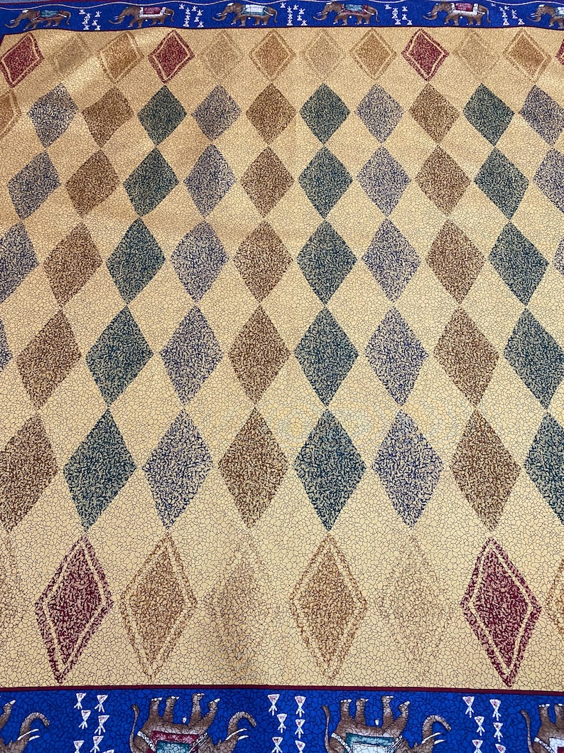 May include: A fabric textile featuring a repeating diamond pattern in shades of dark green, brown, and maroon on a tan background with a fine crackle texture. The top and bottom borders are blue with a repeating graphic of elephants.
