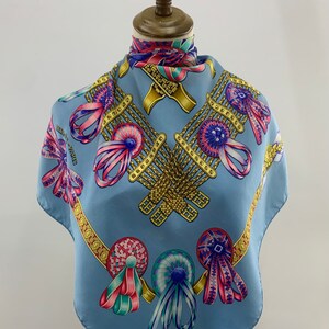 May include: A light blue silk scarf with a pattern of gold chains, colourful ribbons, and rosettes. The scarf is displayed on a mannequin.