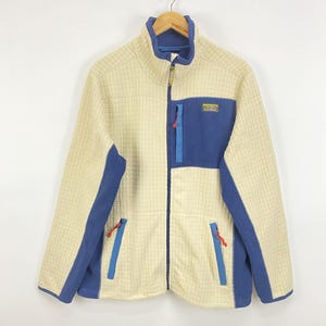 May include: A cream-colored, grid-textured fleece jacket with blue panels on the sides, sleeves, and chest pocket. It features a full-length front zipper, a stand-up collar, and red zipper pulls. An L.L.Bean logo patch is on the chest pocket.