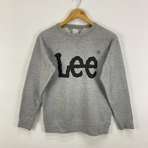 Könnte beinhalten: Ein graues Sweatshirt mit dem Wort "Lee" in großen, schwarzen, stilisierten Buchstaben auf der Brust. Das Sweatshirt hat einen Rundhalsausschnitt und lange Ärmel. Das Lee-Logo ist auch auf dem oberen Rücken sichtbar.