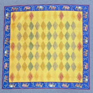 May include: A square scarf featuring a yellow field with a repeating diamond pattern in shades of gold, green, and red. The border is a deep blue with a repeating motif of elephants in profile, each wearing a decorative saddle, and small white icons.
