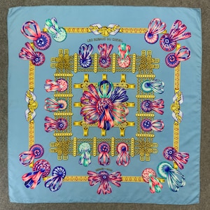 May include: A blue silk scarf with a gold and white pattern of ribbons and bows. The text "Les Rubans du Cheval" is printed in the centre of the scarf.