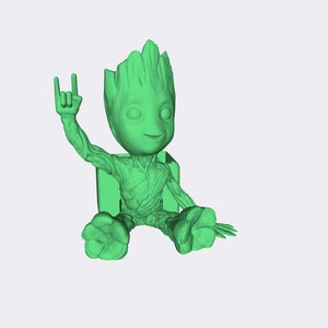 May include: A green figurine of a character from the Guardians of the Galaxy movie franchise. The character is sitting with one arm raised in a rock and roll hand gesture.
