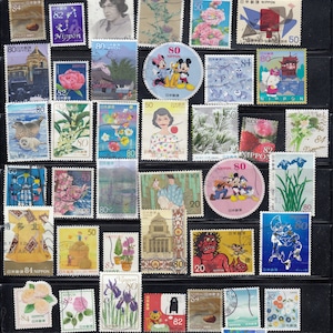 Puede incluir: Una colecci&oacute;n de coloridos sellos postales japoneses, con varios dise&ntilde;os. Los sellos representan flores, retratos, personajes de dibujos animados y paisajes. Los sellos est&aacute;n dispuestos sobre un fondo negro.