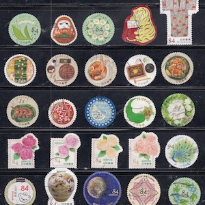 Puede incluir: Una colecci&oacute;n de veinticinco sellos postales japoneses dispuestos en cinco filas. Los sellos presentan diversas ilustraciones que incluyen comida, flores, animales, un kimono y cuerpos celestes, marcados con un valor de 84 o 94 yenes.