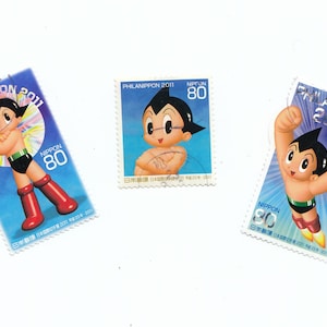 May include: Three postage stamps featuring a cartoon character with black hair and a red suit. The stamps are blue and white with the text "PHILANIPPON 2011" and "NIPPON 80" on each.