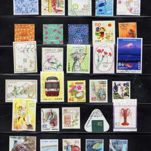 Puede incluir: Una colecci&oacute;n de varios sellos postales japoneses dispuestos en filas, con diversas ilustraciones que incluyen paisajes, animales, figuras culturales, trenes y dise&ntilde;os florales, cada uno marcado con su valor en yenes.