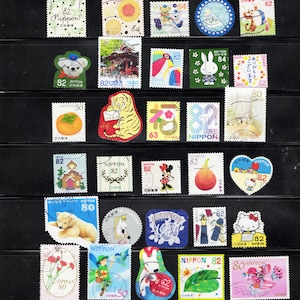 Puede incluir: Una colecci&oacute;n de varios sellos postales japoneses dispuestos en filas, con diversas ilustraciones que incluyen animales, frutas, flores, personajes de dibujos animados y escenas tradicionales, con denominaciones como 50, 62, 63, 80, 82 y 84.