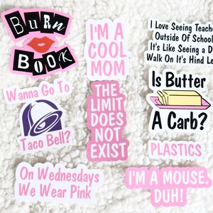 Op de afbeelding: Een set van negen roze en witte stickers met verschillende spreuken en afbeeldingen. De stickers omvatten: "Burn Book", "I'm a Cool Mom", "The Limit Does Not Exist", "Wanna Go To Taco Bell?", "On Wednesdays We Wear Pink", "I Love Seeing Teachers Outside Of School, It's Like Seeing a Dog Walk On It's Hind Legs. Is Butter A Carb?", "Plastics", "I'm a Mouse. Duh!"