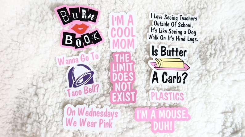 Op de afbeelding: Een set van negen roze en witte stickers met verschillende spreuken en afbeeldingen. De stickers omvatten: "Burn Book", "I'm a Cool Mom", "The Limit Does Not Exist", "Wanna Go To Taco Bell?", "On Wednesdays We Wear Pink", "I Love Seeing Teachers Outside Of School, It's Like Seeing a Dog Walk On It's Hind Legs. Is Butter A Carb?", "Plastics", "I'm a Mouse. Duh!"