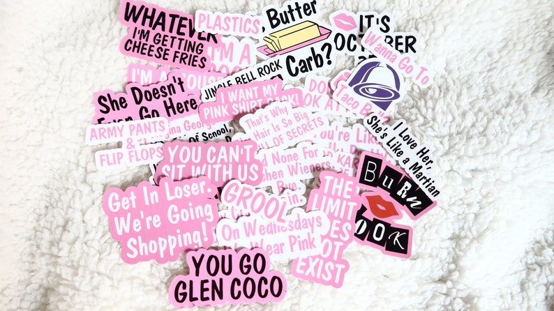 Op de afbeelding: Een verzameling roze en witte stickers met verschillende zinnen en afbeeldingen. De stickers bevatten tekst zoals "Whatever I'm getting cheese fries", "I'm a Jingle Bell Rock", "You can't sit with us", "Get in loser, we're going shopping", "Grool", "The Limit Does Not Exist", "You go Glen Coco", "I love her, she's like a Martian", "Burr", "It's October, wanna go to Taco Bell", "Do you want my pink shirt?", "That's why hair is so big, full of secrets", "And none for you,  'cause you're like,  'She's like a Martian'" and "On Wednesdays we wear pink".