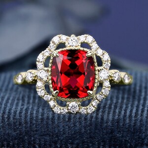 May include: A gold ring featuring a large, red, square-shaped gemstone encircled by a halo of smaller diamonds.