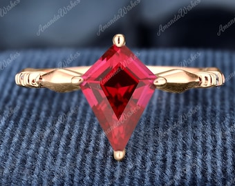 May include: A rose gold ring with a square-shaped, red gemstone set in the center. The ring has a delicate design with curved accents on either side of the stone.